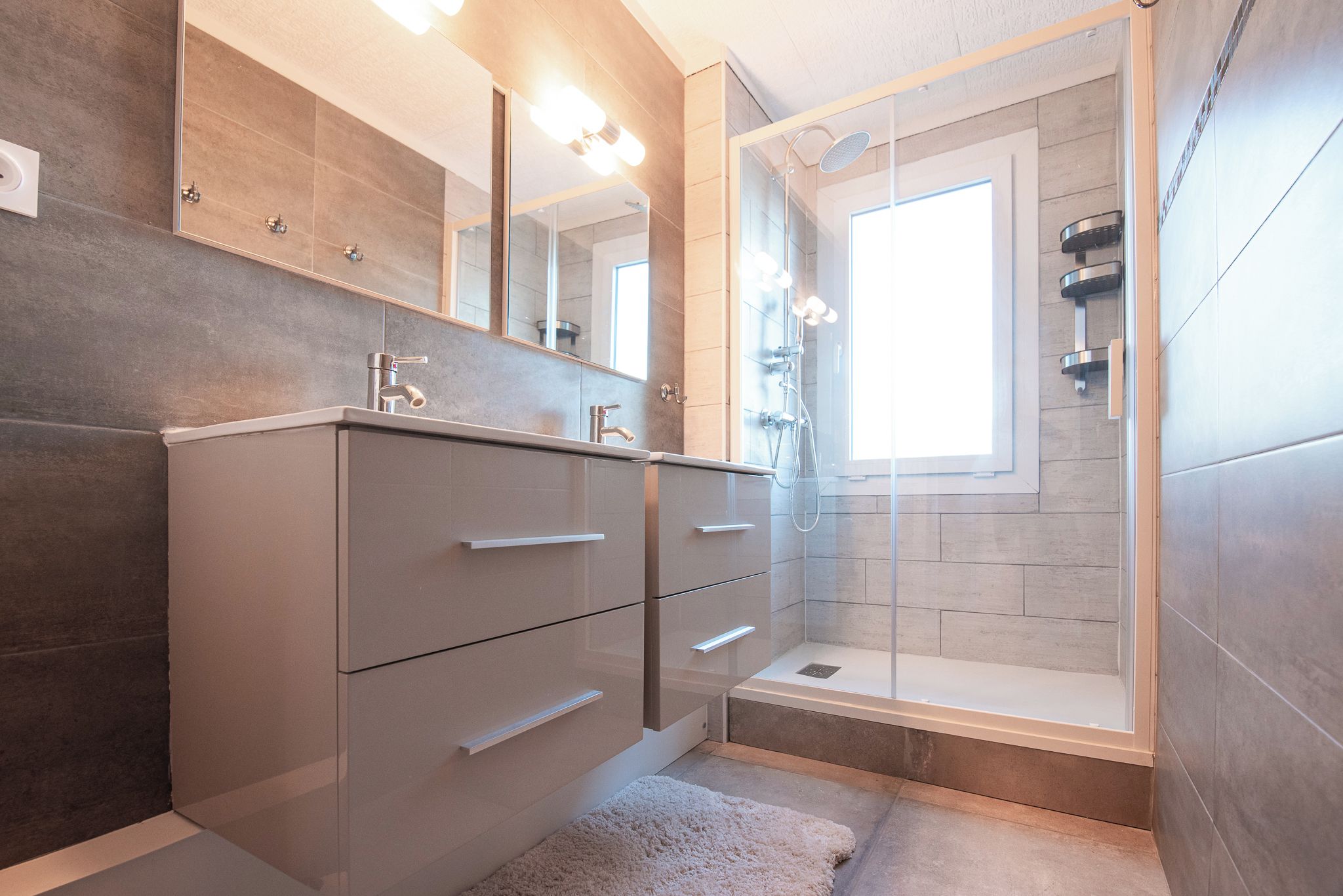 A modern bathroom with a walk-in shower, a large mirror, and a built-in vanity with drawers.