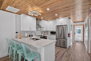 A modern kitchen with white cabinetry, a stainless steel refrigerator, and a wooden ceiling. - Tides & Turtles · Canal Dock · Waterfront (Holmes Beach)