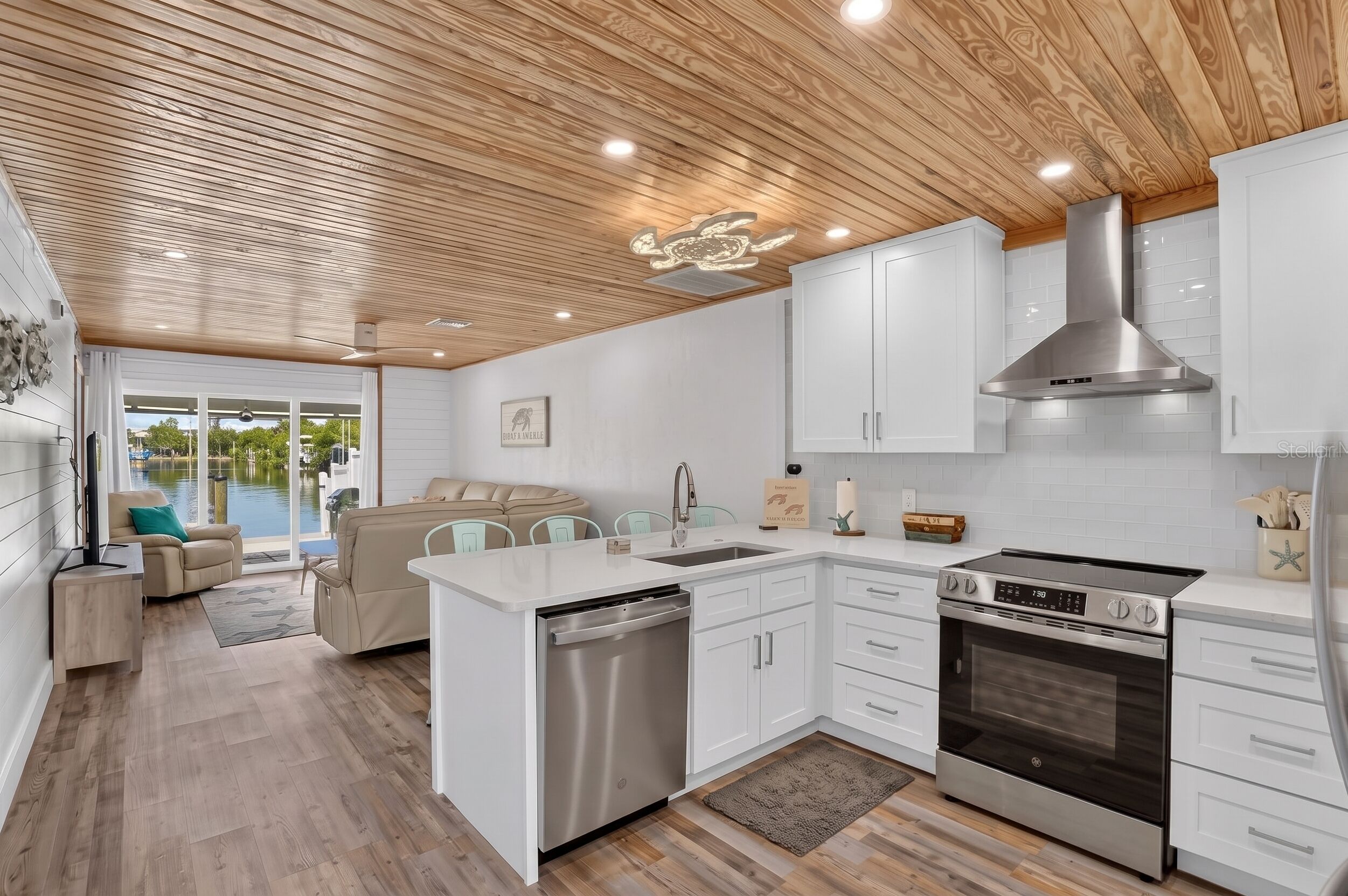 A modern kitchen with white cabinetry, a stainless steel oven, and a wooden ceiling.