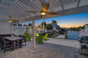 An outdoor patio with a table and chairs, a grill, and a view of a marina. - Tides & Turtles · Canal Dock · Waterfront (Holmes Beach)