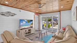 Una sala de estar con televisor, sofás beige y techo de madera.