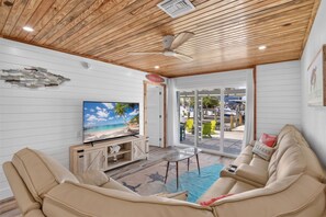 Ein Wohnzimmer mit Fernseher, beigen Sofas und einer Holzbalkendecke.