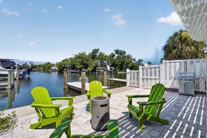 Eine Uferterrasse mit grünen Adirondack-Stühlen, einem Grill und einem Mülleimer.