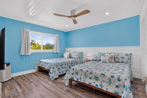 A bedroom with two beds, a ceiling fan, a TV, and a window with curtains. - Tides & Turtles · Canal Dock · Waterfront (Holmes Beach)