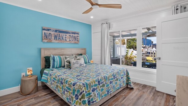 Un dormitorio con una cama, un ventilador de techo, una ventana con cortinas y un cartel en la pared que dice 'NO WAKE ZONE'.