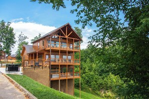A multi-story wooden cabin with balconies, surrounded by lush greenery. - Jump on Inn to this luxurious new pool cabin. (Sevierville)