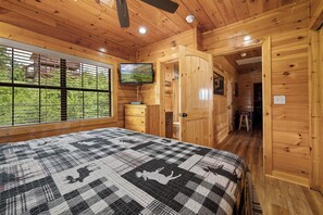 A wooden cabin bedroom with a bed, dresser, TV, and a view of greenery outside. - Amazing View Lodge is a spectacular seven-bedroom cabin (Sevierville)