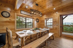 A wooden cabin interior with a dining table set for four, a clock, and a sign that reads 'the Mountains are calling.' - Amazing View Lodge is a spectacular seven-bedroom cabin (Sevierville)
