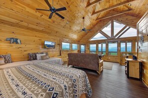 A log cabin bedroom with a bed, a chair, a desk, and a television. - One Bedroom 2 Story Log Cabin with Panoramic Views! (Sevierville)