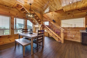 A wooden cabin interior with a dining table, chairs, a staircase, and a view of the outside. - One Bedroom 2 Story Log Cabin with Panoramic Views! (Sevierville)