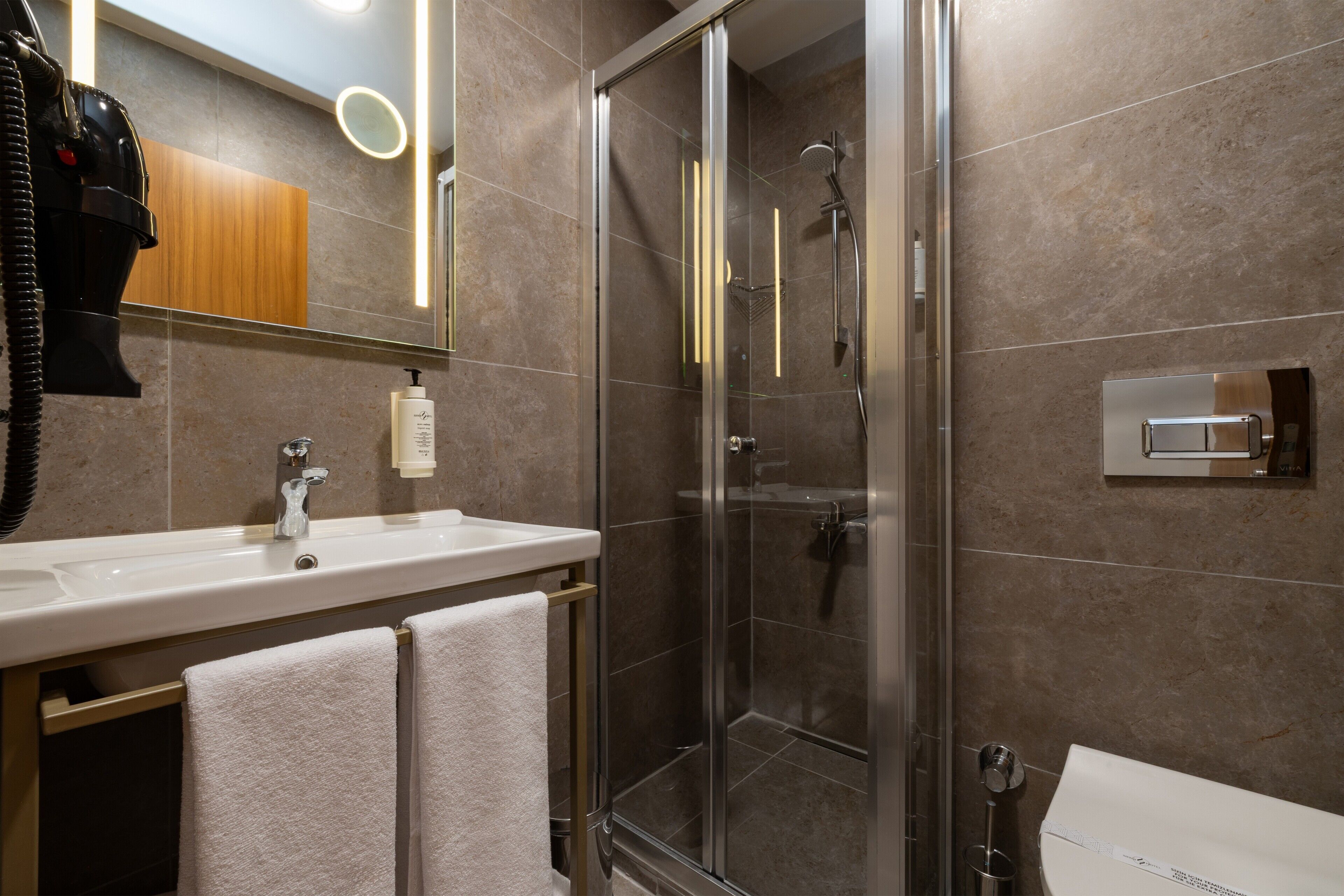 A modern bathroom with a glass-enclosed shower, a white sink, and a mirror with a wooden cabinet above.