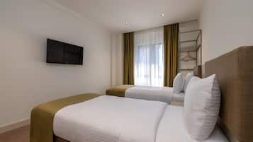 Een hotelkamer met twee bedden, een aan de muur bevestigde televisie en een raam met gordijnen.