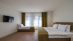 Habitación de hotel con cama, sofá, televisión y ventana con cortinas.