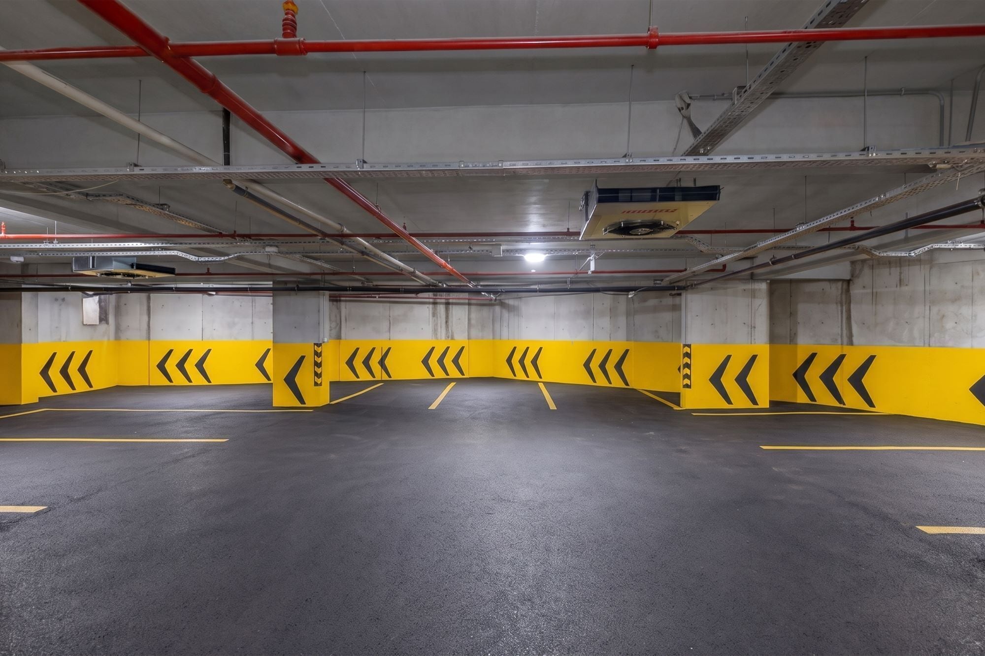 Un estacionamiento vacío con barreras de seguridad amarillas y flechas direccionales en el suelo.