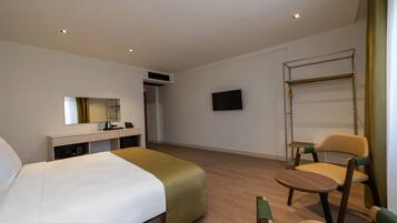 A hotel room with a bed, a desk with a mirror, a television, a chair, and a small table.