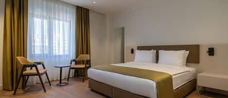 A hotel room with a large bed, two chairs, a small table, and a bedside table.