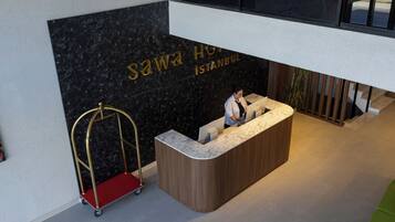 A reception desk with a marble top, a black marble wall with the hotel name, and a red luggage cart.