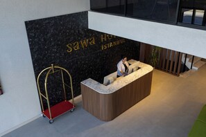 A reception desk with a marble top, a black marble wall with the hotel name, and a red luggage cart.