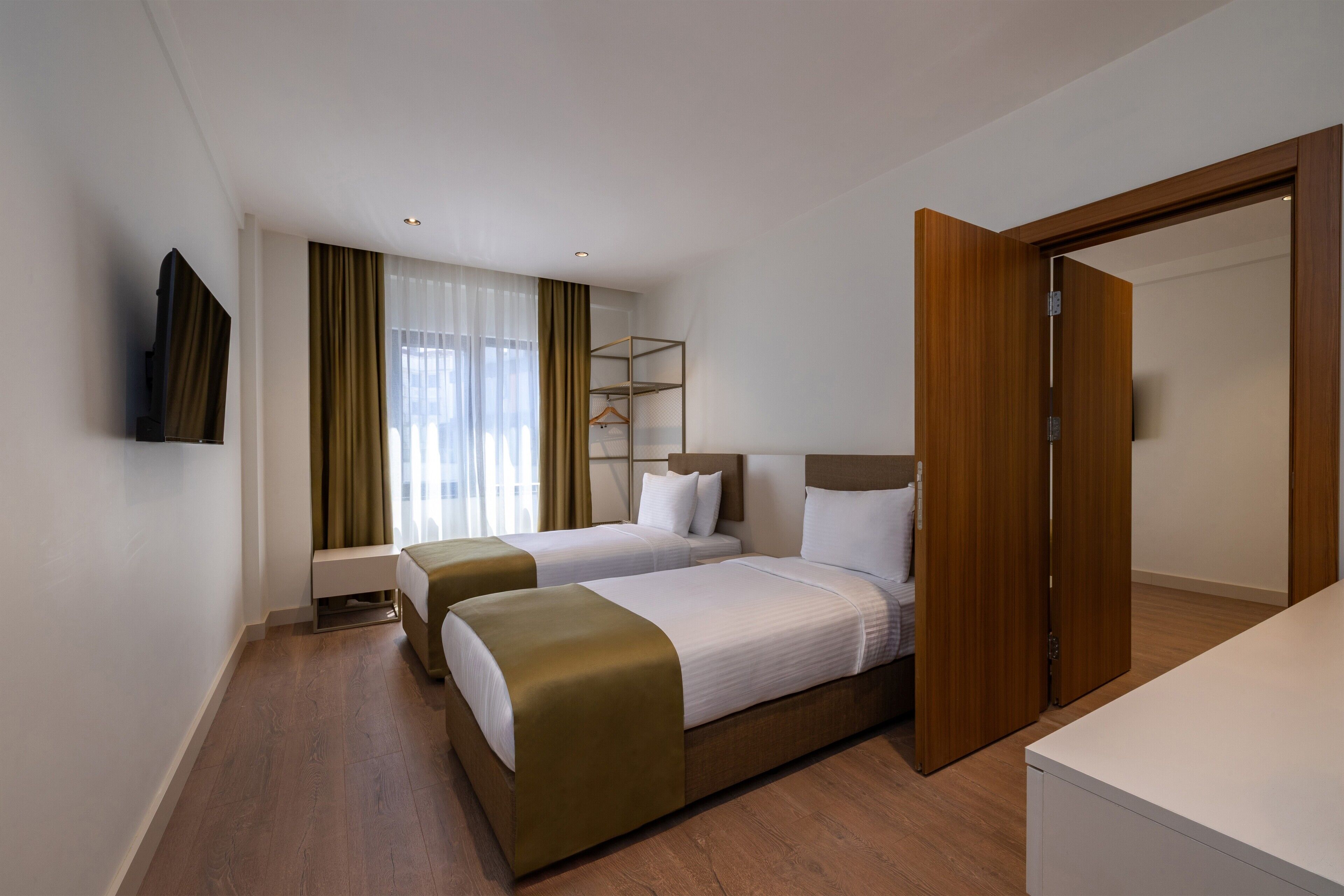 A hotel room with two beds, a bedside table, a wardrobe, and a television on the wall.