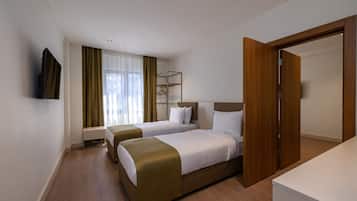 A hotel room with two beds, a bedside table, a wardrobe, and a television on the wall.
