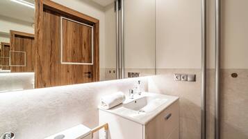 A modern bathroom with a white sink, a mirror, and a shower area.