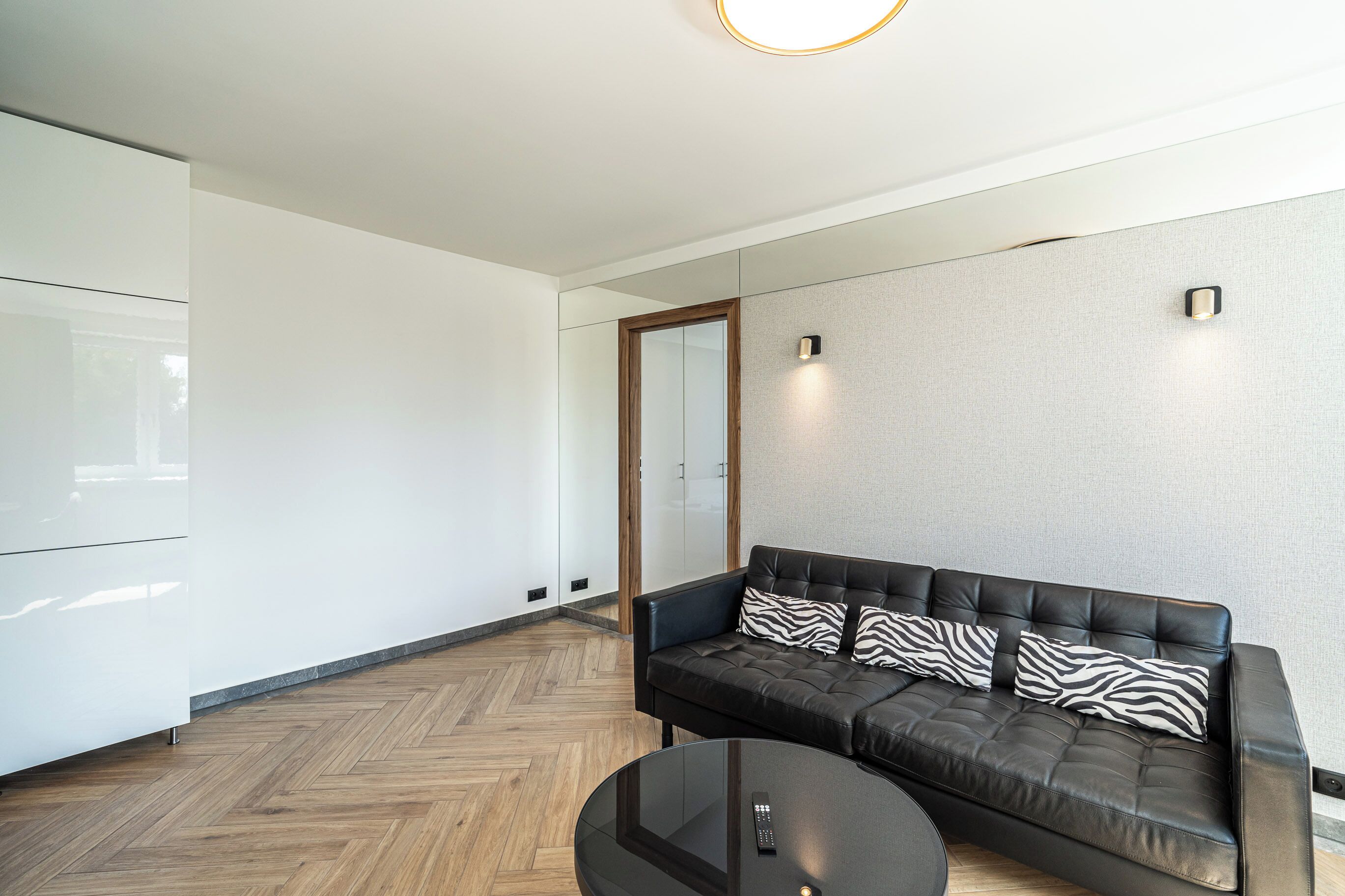 Una sala moderna con un sofá de cuero, una mesa de centro de vidrio y un piso de madera con diseño en espiga.