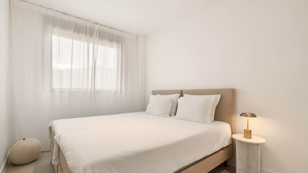 A minimalist bedroom with a bed, a bedside lamp, and a round ottoman. - RDR577 - Designer 2-Bed with Garden in Camarate Hills (Buenas Noches)
