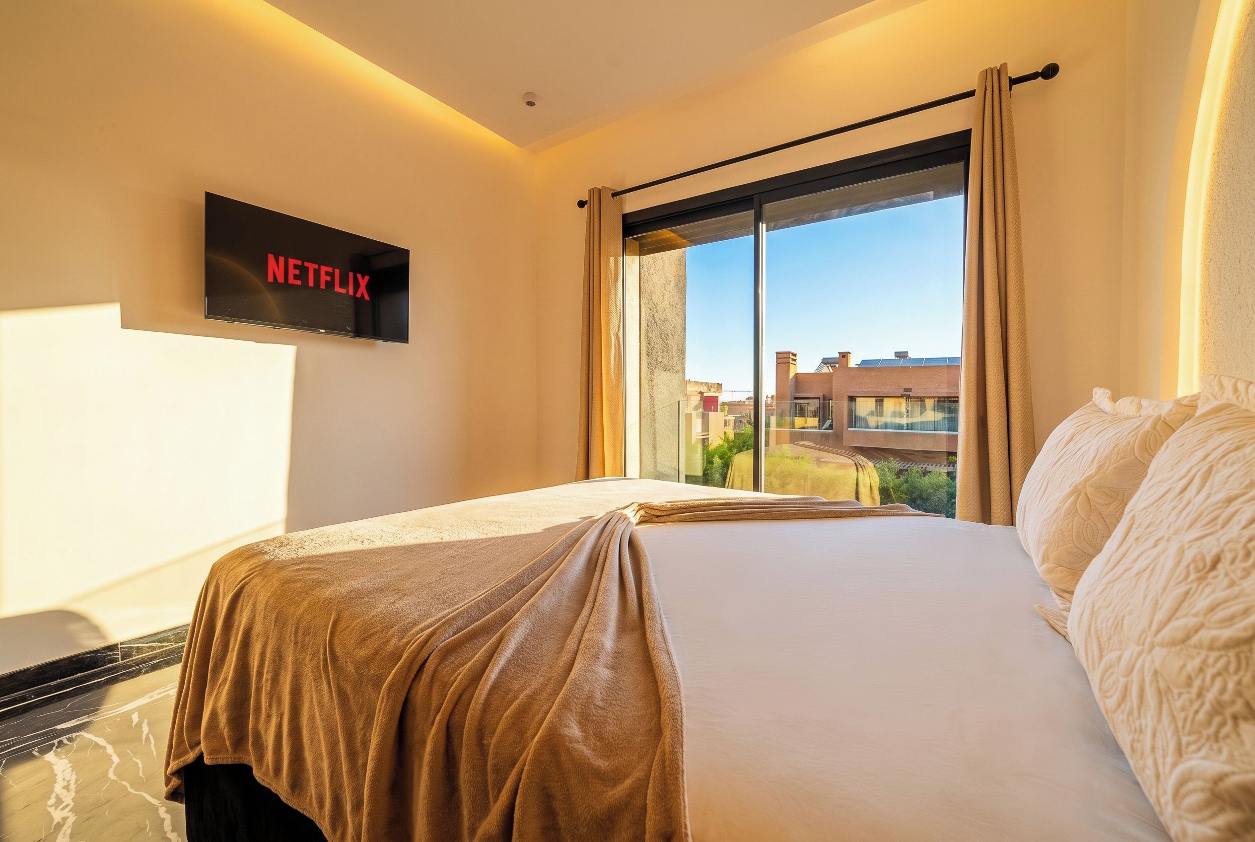 Een hotelkamer met een bed, een aan de muur bevestigde televisie en een groot raam met gordijnen.