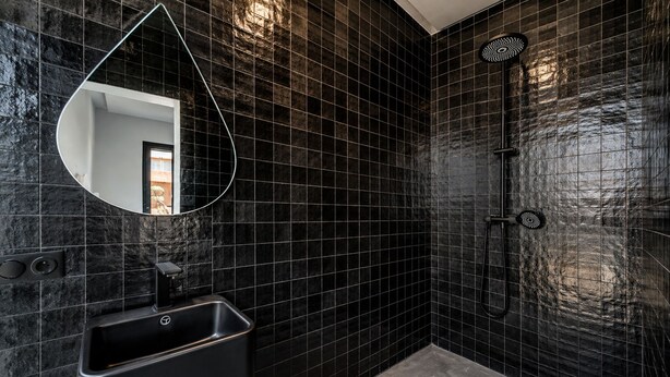 Een moderne badkamer met zwart betegelde wanden, een enkele wastafel en een douche.