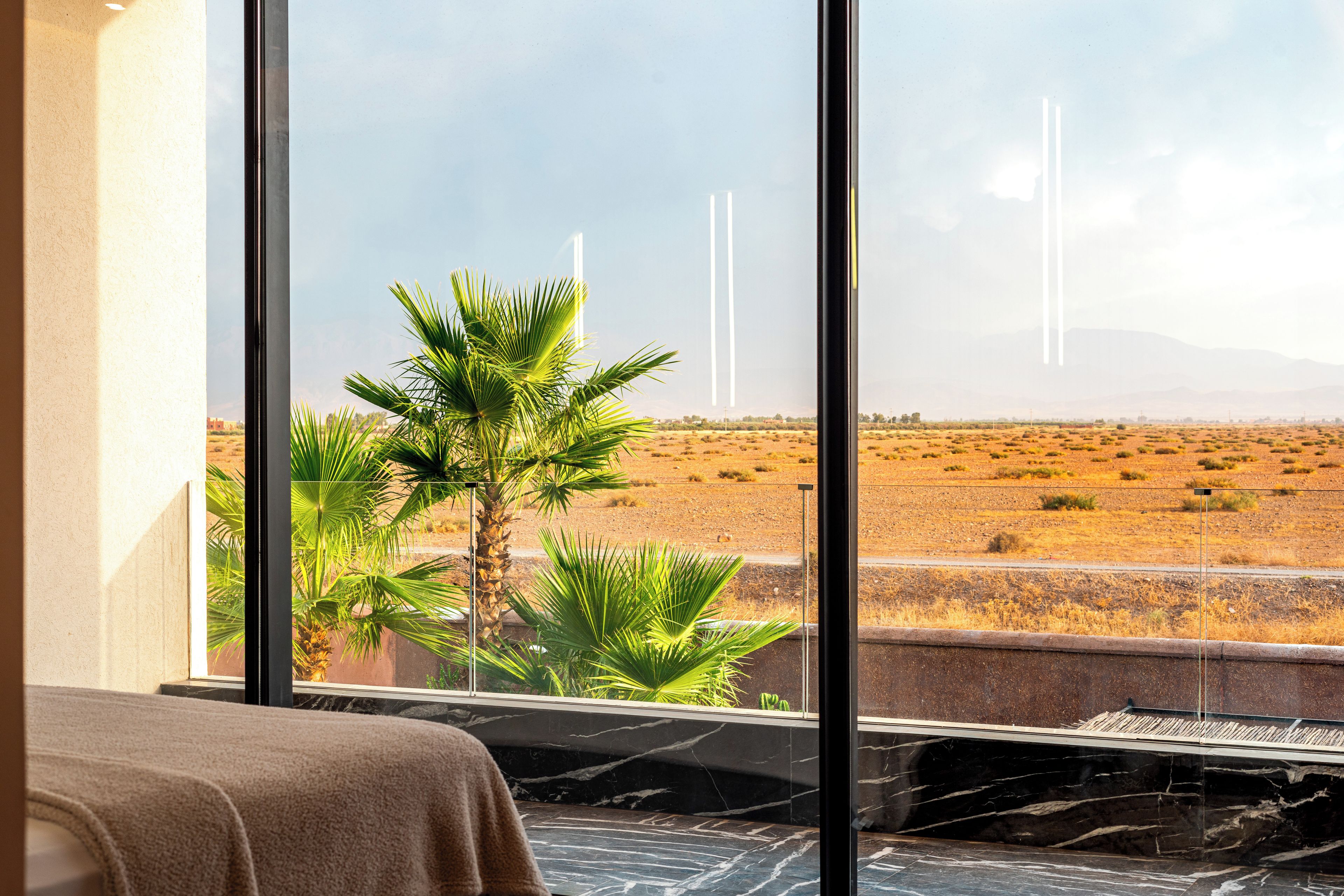 A room with a large window overlooking a desert landscape with palm trees and distant mountains.