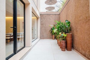 Een smalle gang met een glazen deur die uitkomt in een eetruimte, omringd door potplanten en een structuurwand.