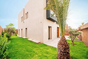 A modern building with a flat facade, a small entrance, and a well-maintained lawn with a palm tree. - Villa with Pool, Jacuzzi, Sauna, and Hammam in Marrakech (Marrakech)