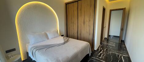 A modern bedroom with a curved headboard, a wooden wardrobe, and a marble floor.