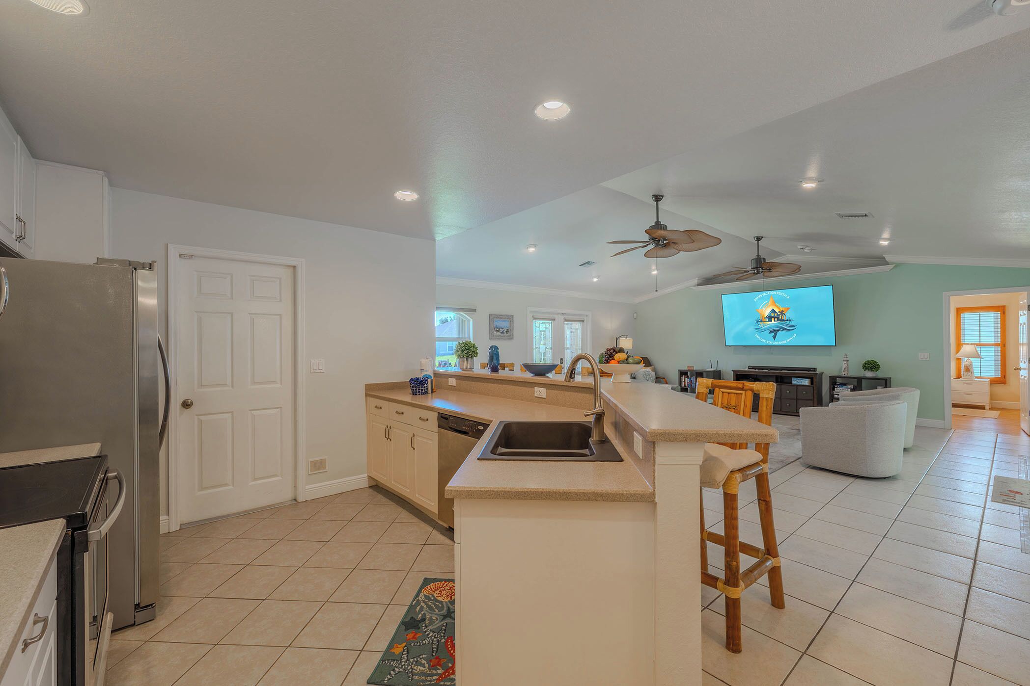 A modern kitchen with a central island, a refrigerator, and a dining area with a television.