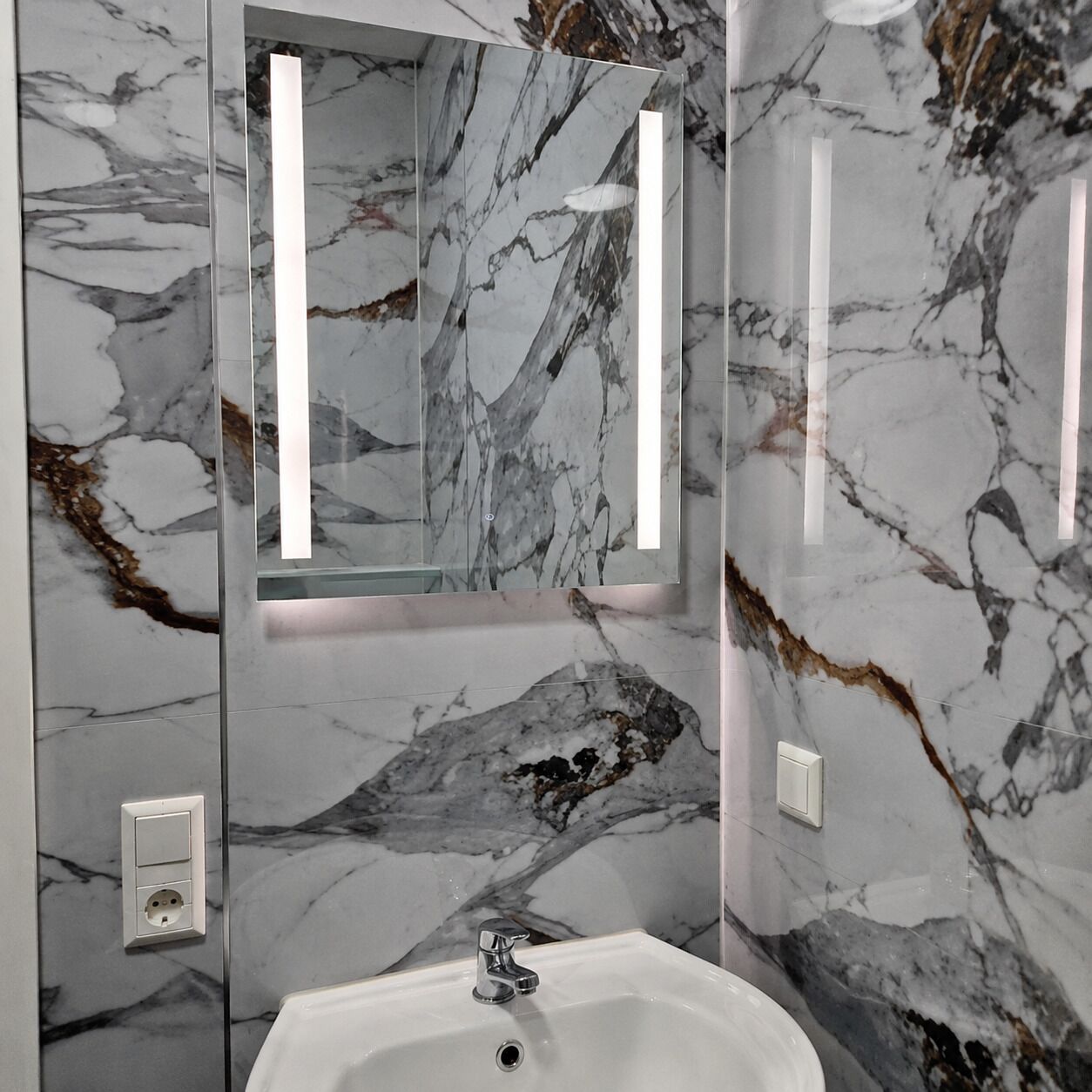 A bathroom with a marble wall, a sink, and a mirror.