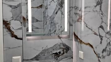 A bathroom with a marble wall, a sink, and a mirror.