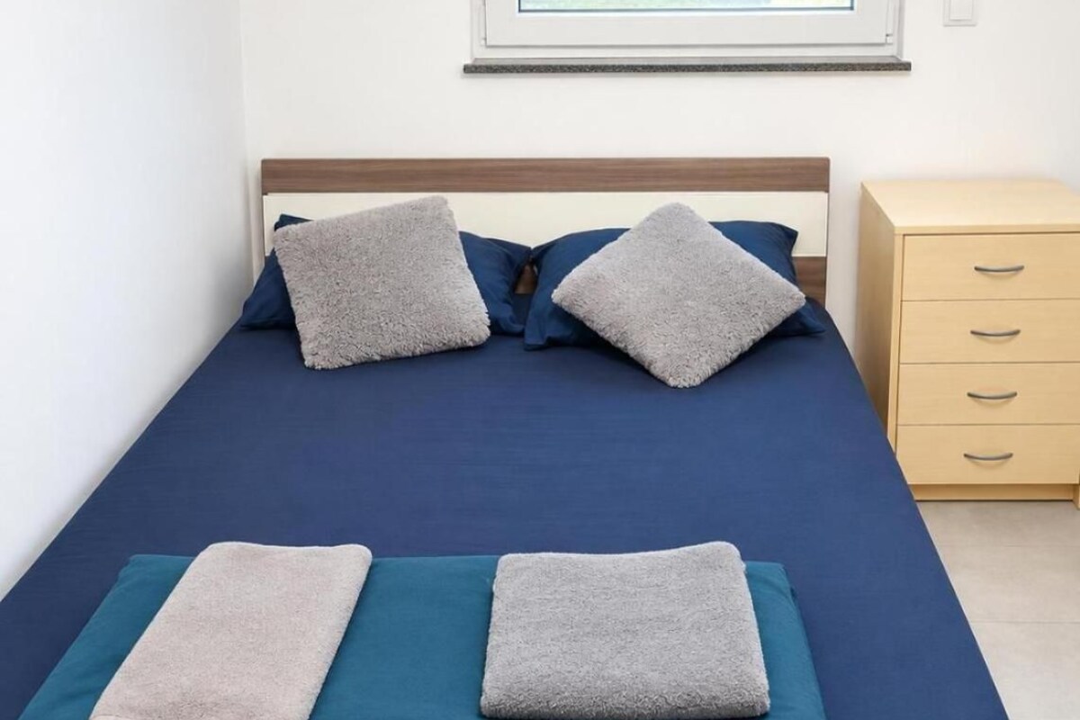 Una cama con un colchón azul, dos almohadas grises y dos toallas dobladas.