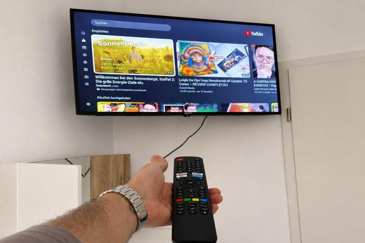 Una persona sostiene un control remoto frente a un televisor que muestra varios canales.