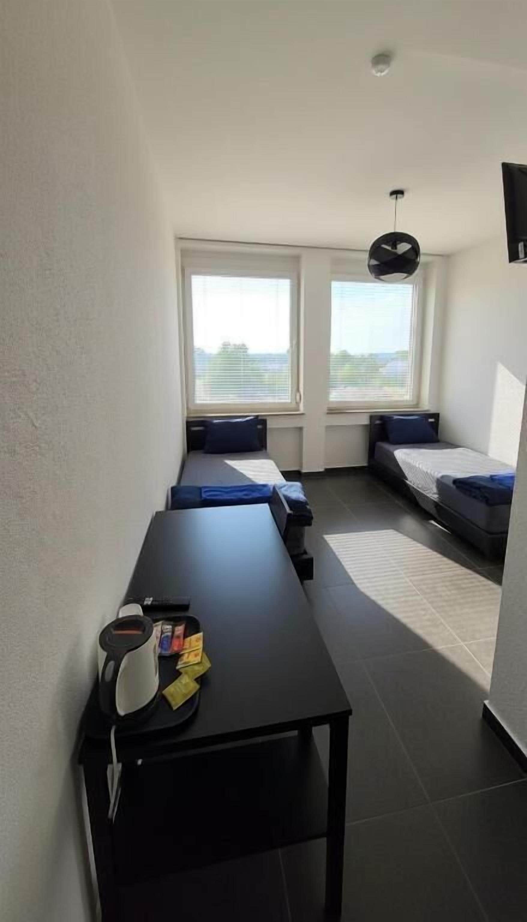A compact room with a long table, two beds with blue bedding, and a ceiling fan.