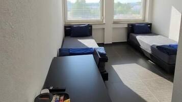 A compact room with a long table, two beds with blue bedding, and a ceiling fan.