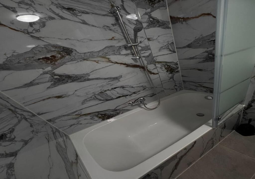 Une salle de bain avec un mur en marbre, une baignoire et un espace douche.