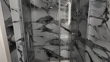 A bathroom with a marble wall, a shower, and a mirror.