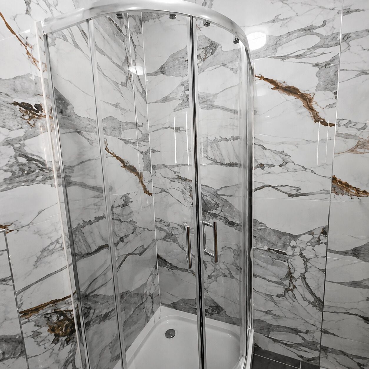 Een douche met glazen wanden en een marmeren muur.