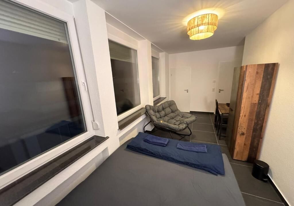 Ein Zimmer mit einem Bett, einem Sessel, einer Holzpaneelausstattung an der Wand und einer Deckenleuchte.