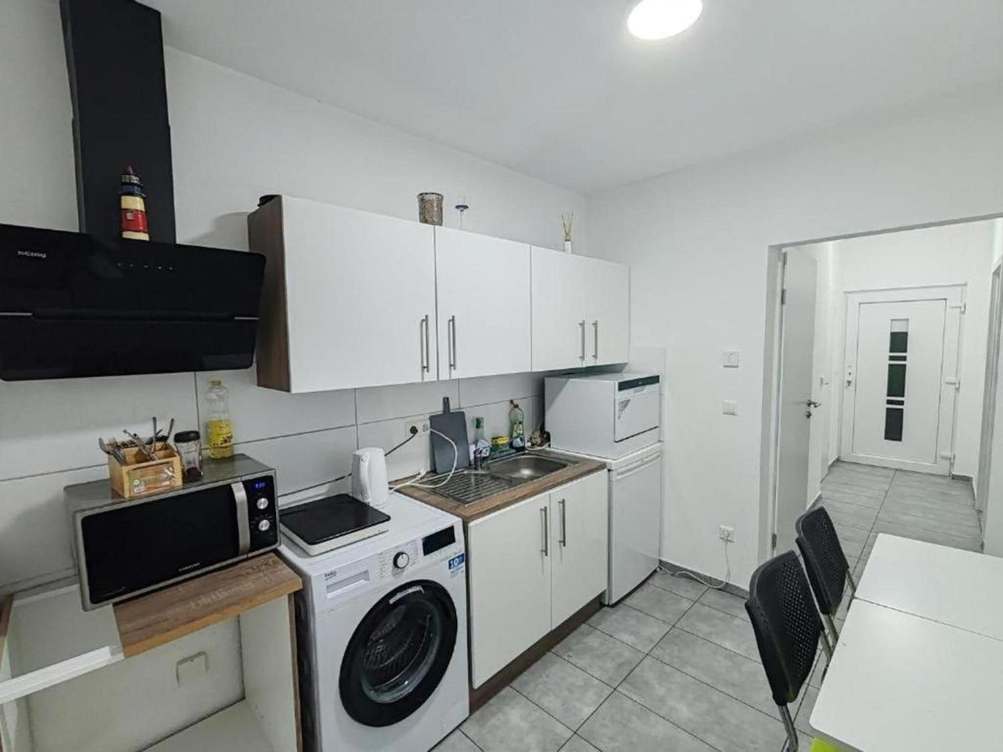 Een kleine keuken met een wasmachine, magnetron en een klein spoelgedeelte.
