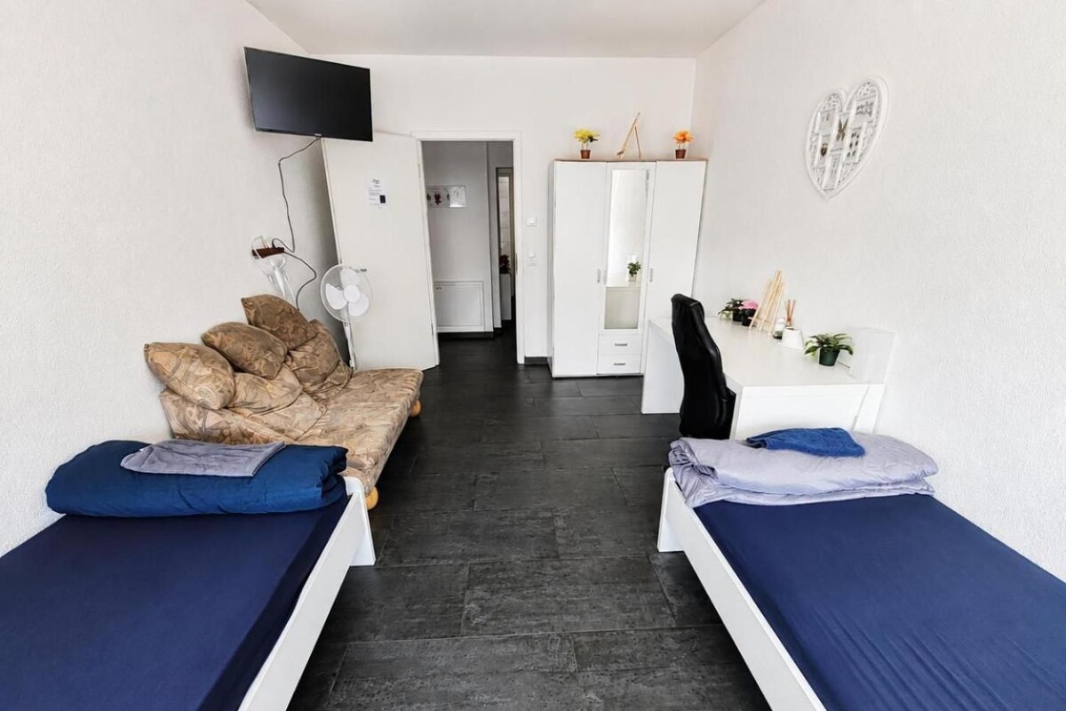 Una habitación con dos camas individuales, un sofá, un escritorio con silla, un televisor y un armario.