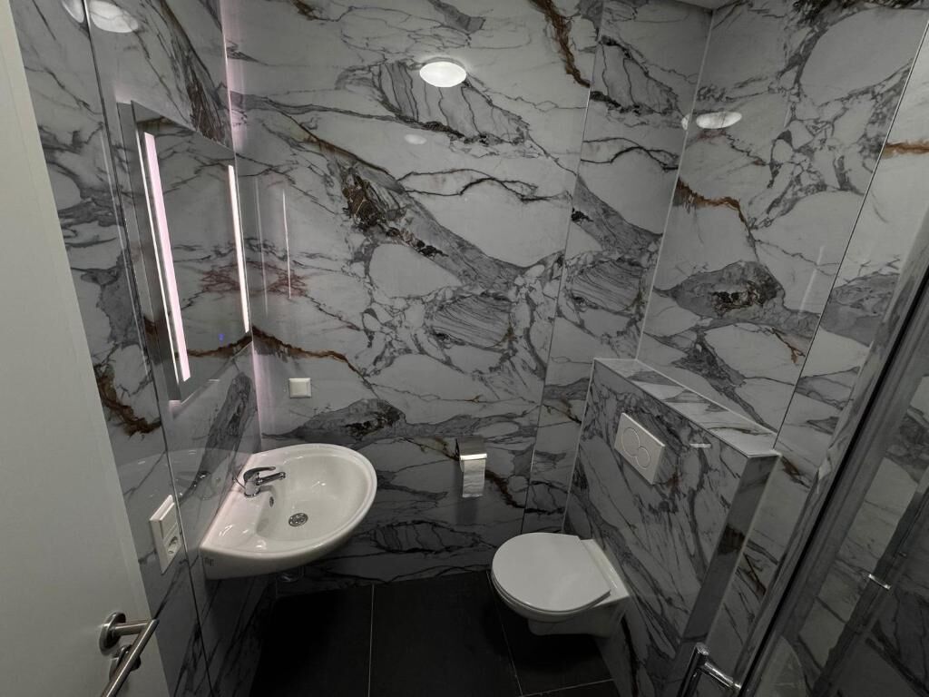Un baño con un lavamanos blanco, inodoro y zona de ducha con mampara de vidrio.