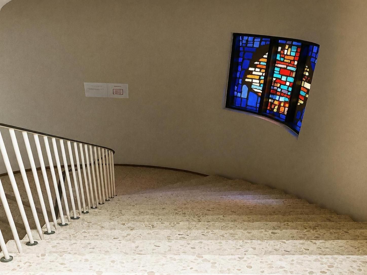 A staircase with a white railing and a stained glass window on the wall.