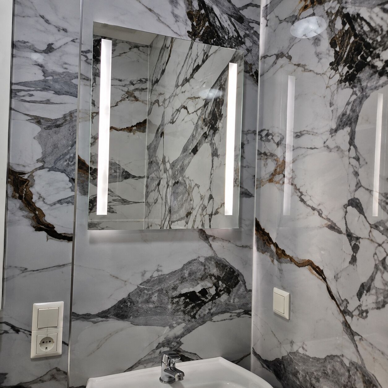 Baño con pared de mármol, lavabo y espejo.