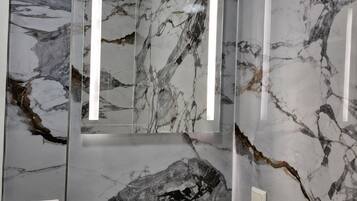 Baño con pared de mármol, lavabo y espejo.